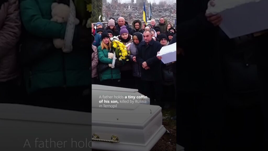 A father gently rocks the small coffin of his one-year-old son.